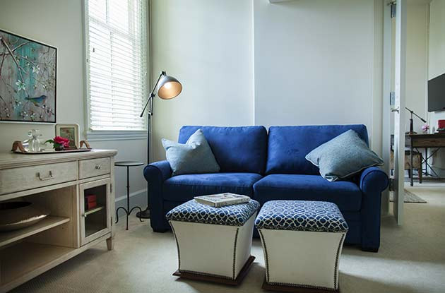 A living room with a blue couch and two blue, patterned ottomans.
