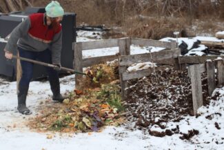 A man turns a compost pile with a pitchfork.